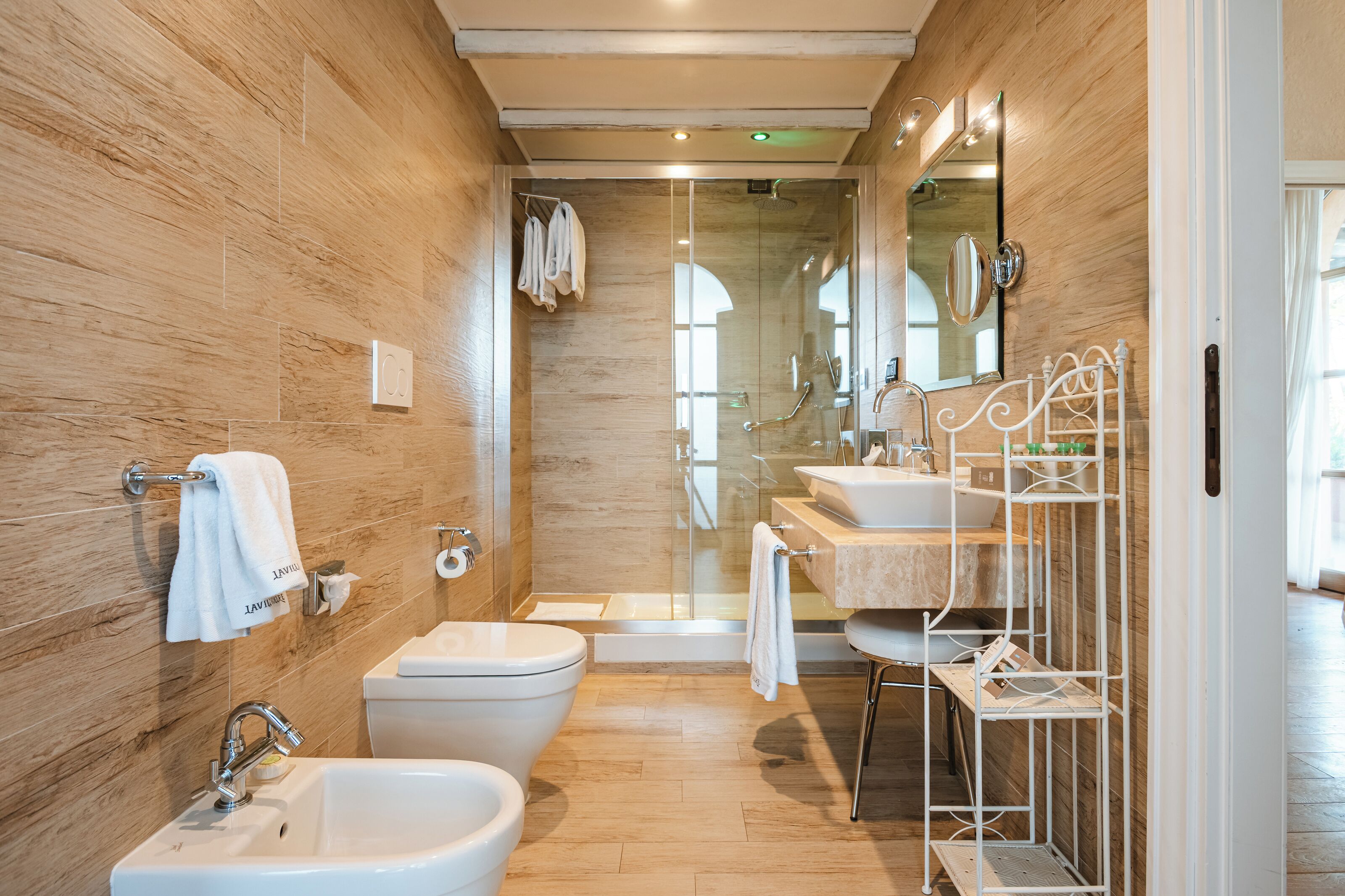 Ein modernes Badezimmer mit einer Holzwand, einer Glasdusche, einem weißen Waschbecken und einem Bidet.