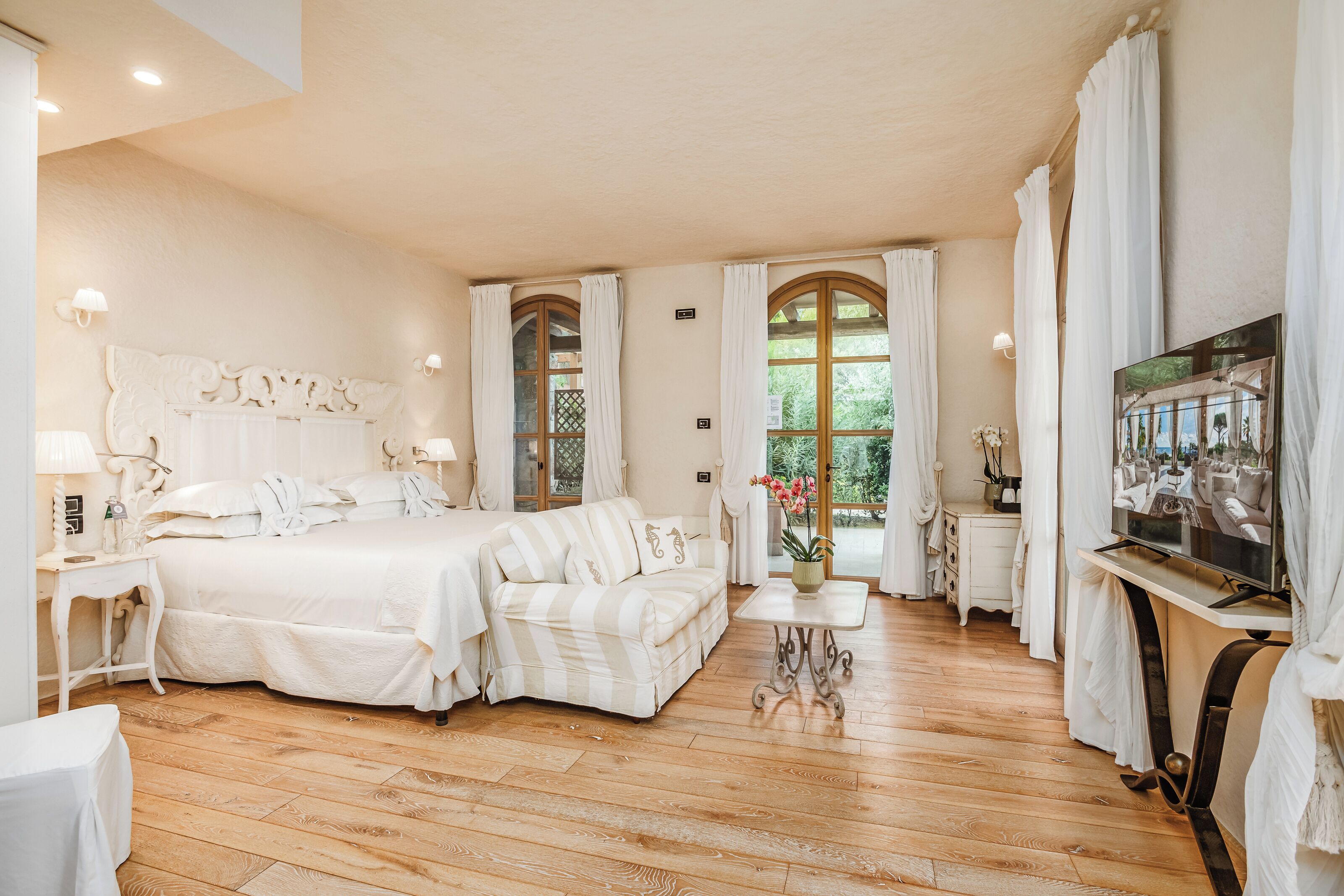 A bedroom with a large bed, a desk, a TV, and a window with curtains.