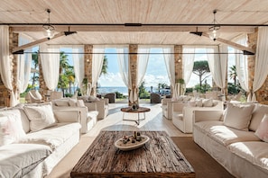 A spacious outdoor seating area with white sofas and a rustic coffee table, set against a backdrop of stone walls and a view of the sea.