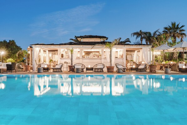 A poolside area with lounge chairs, a bar, and a building with a covered seating area.