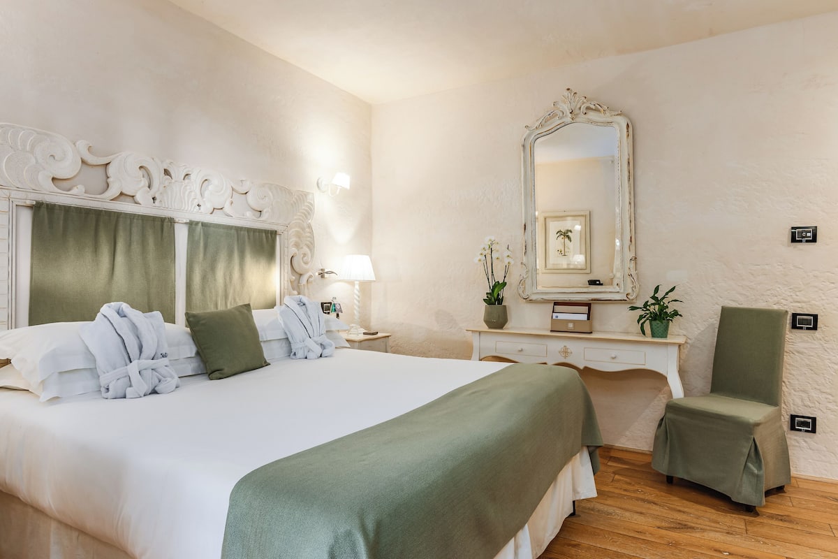 A hotel room with a large bed, a vanity with a mirror, and a chair.