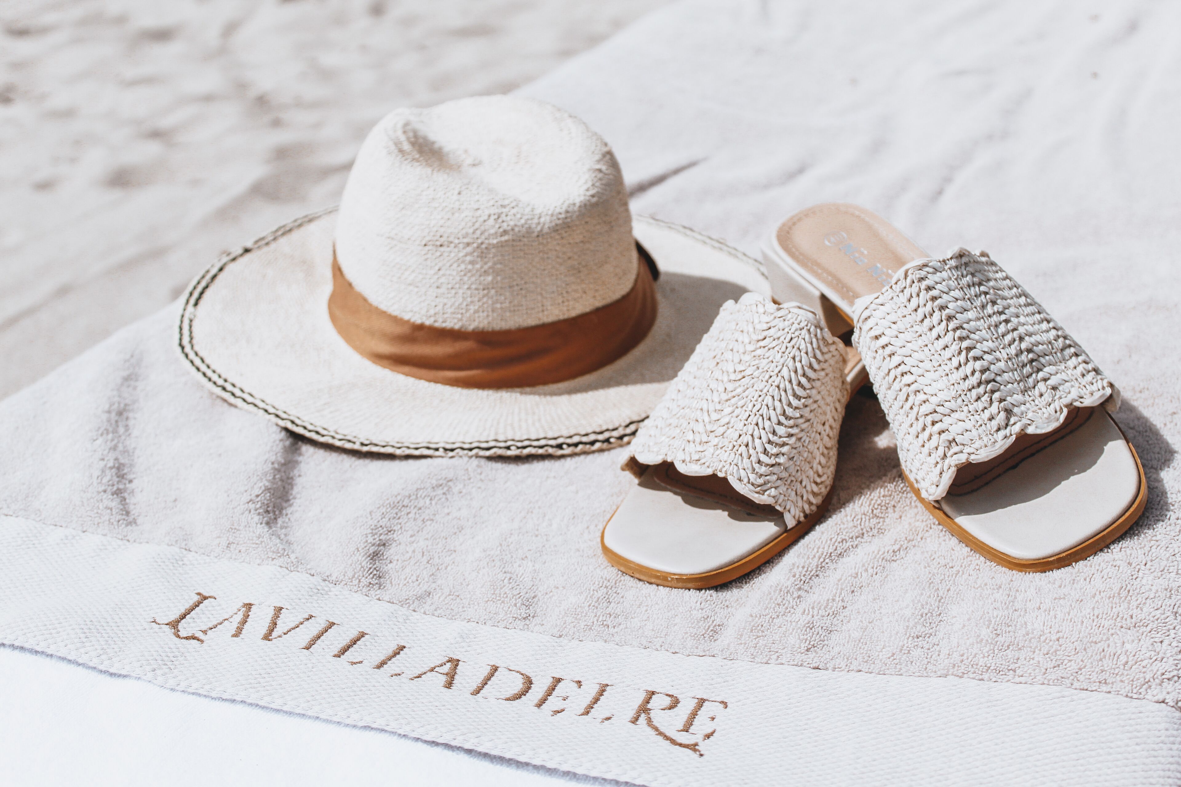 Un chapeau et des sandales posés sur une serviette, avec le texte « LAVILLADELEIRE ».