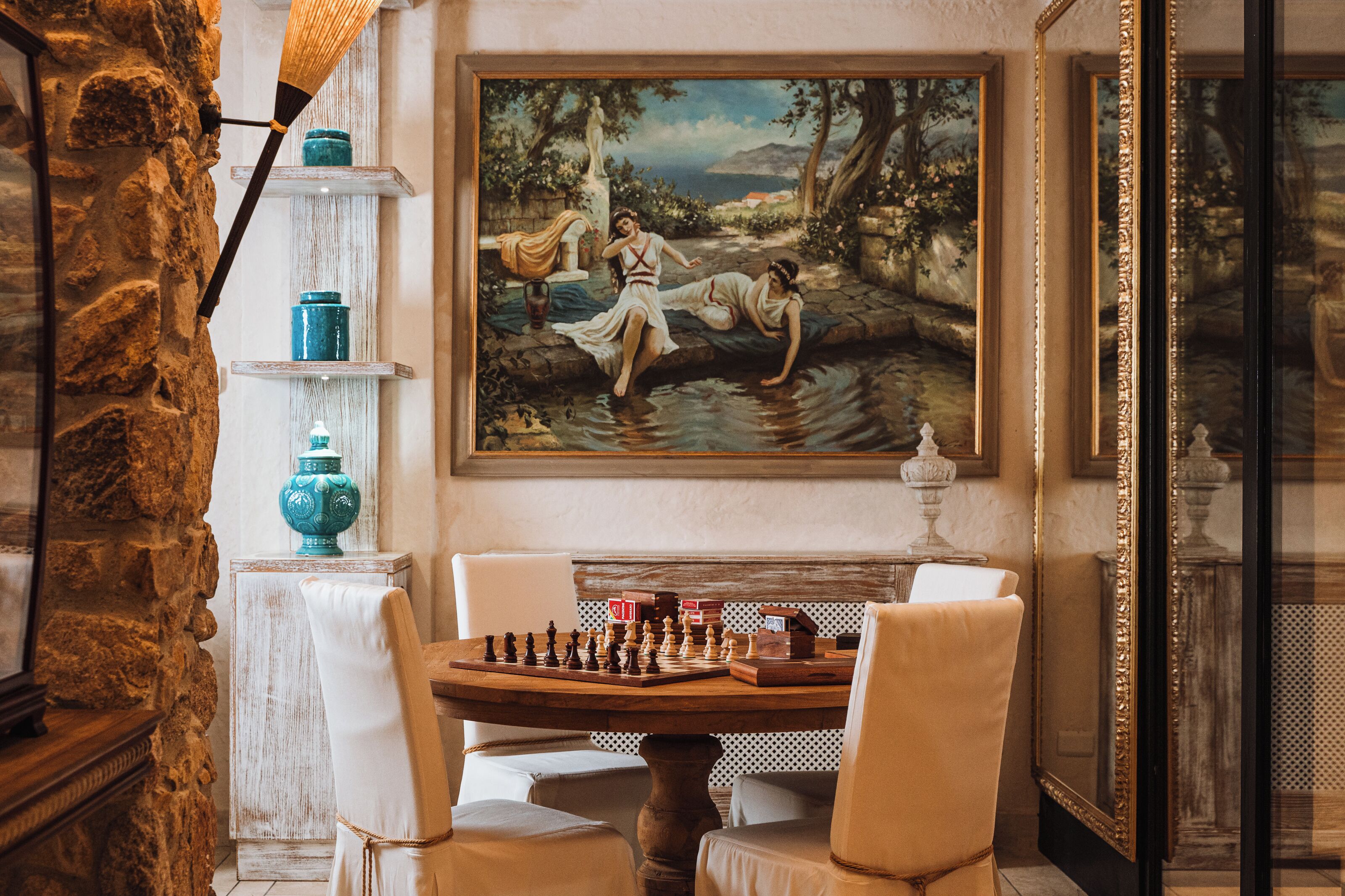 A room with a stone wall, a chessboard on a wooden table, and a classical painting on the wall.