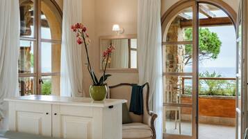 A bathroom with a large arched window, a vanity with a green vase, and a chair by the window.