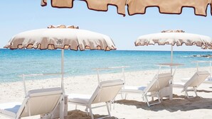 A beach with white lounge chairs and beige umbrellas.