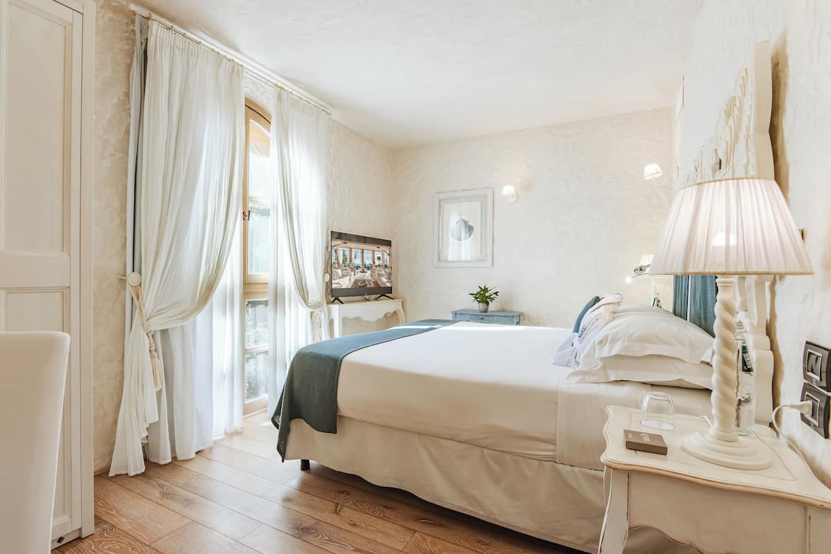 A bedroom with a bed, bedside table, lamp, and a painting on the wall.