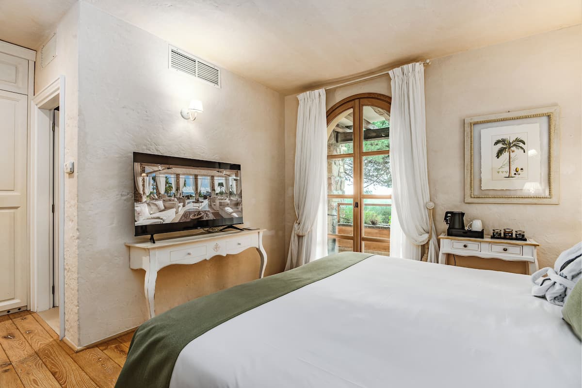 A bedroom with a bed, a television on a dresser, a coffee maker, and a framed picture on the wall.