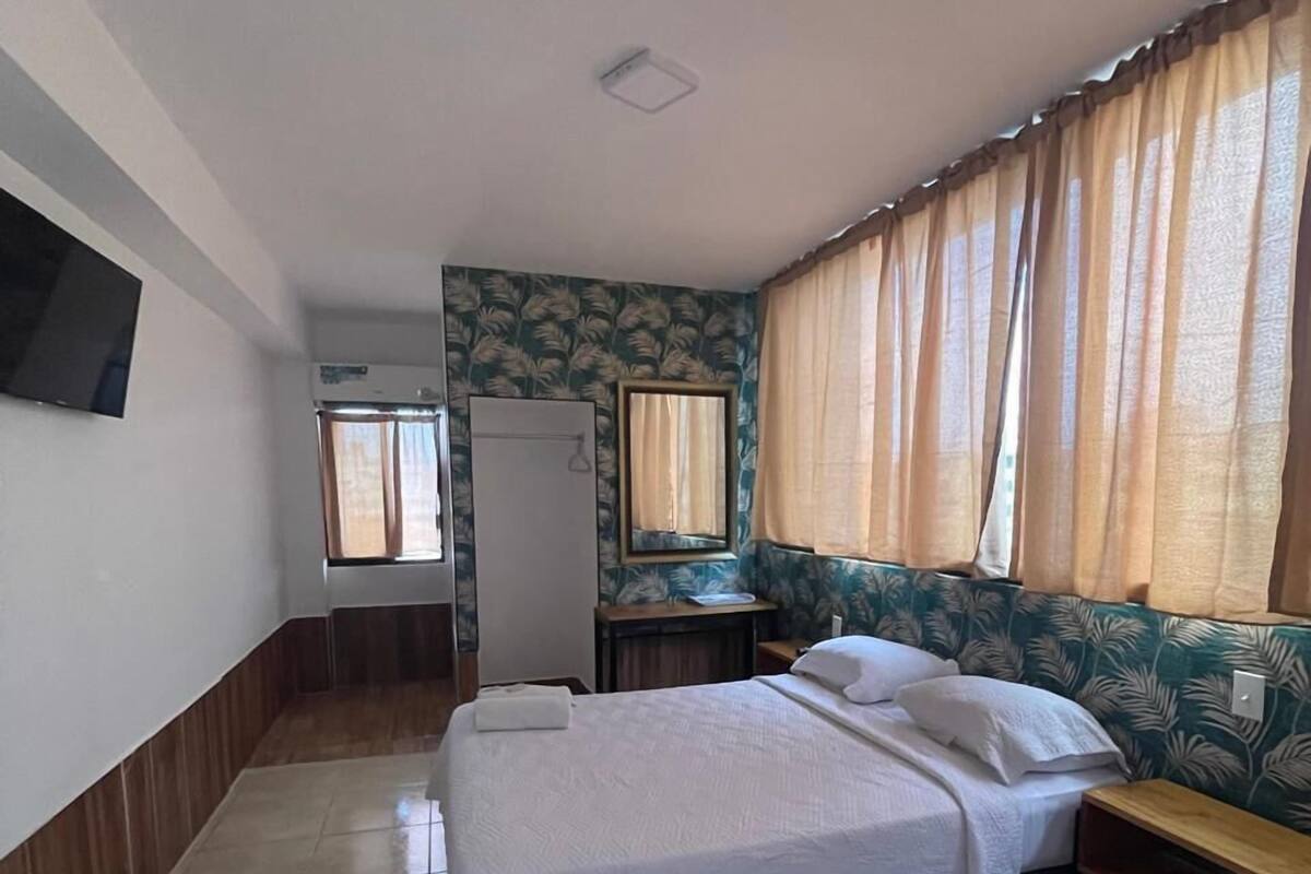 A hotel room with a bed, a desk, a mirror, and a wardrobe.