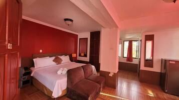 A hotel room with a bed, a sofa, a mirror, a wardrobe, and a refrigerator.