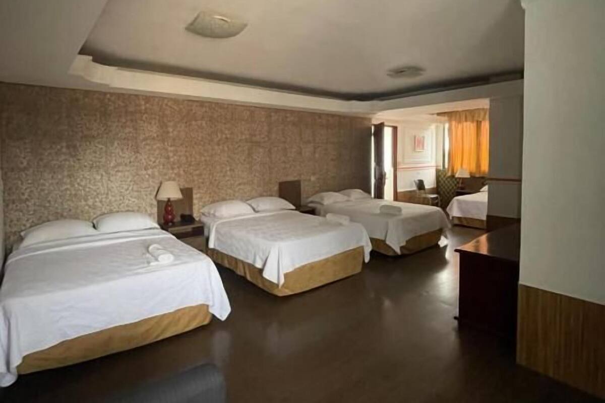 A hotel room with four single beds, a desk, and a large window.