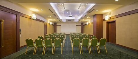 A conference room with rows of green chairs and a large screen at the front.