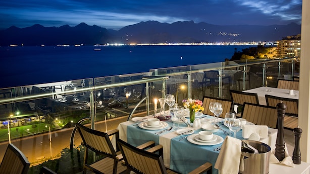 Un comedor con una mesa dispuesta para dos personas, con vista a un cuerpo de agua y montañas lejanas.
