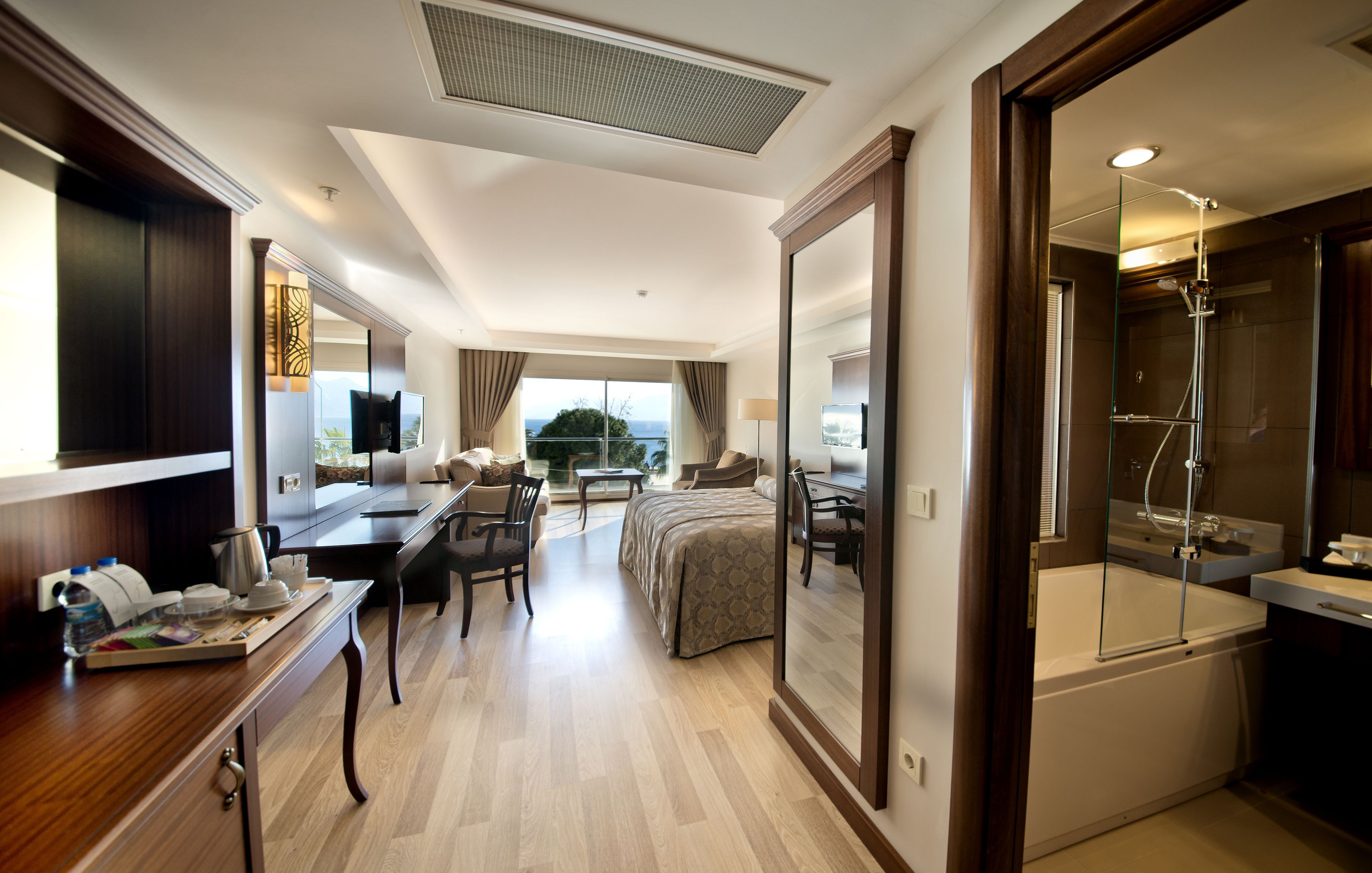 A hotel room with a bed, a desk, a chair, a TV, a bathroom with a shower, and a large window with a view.