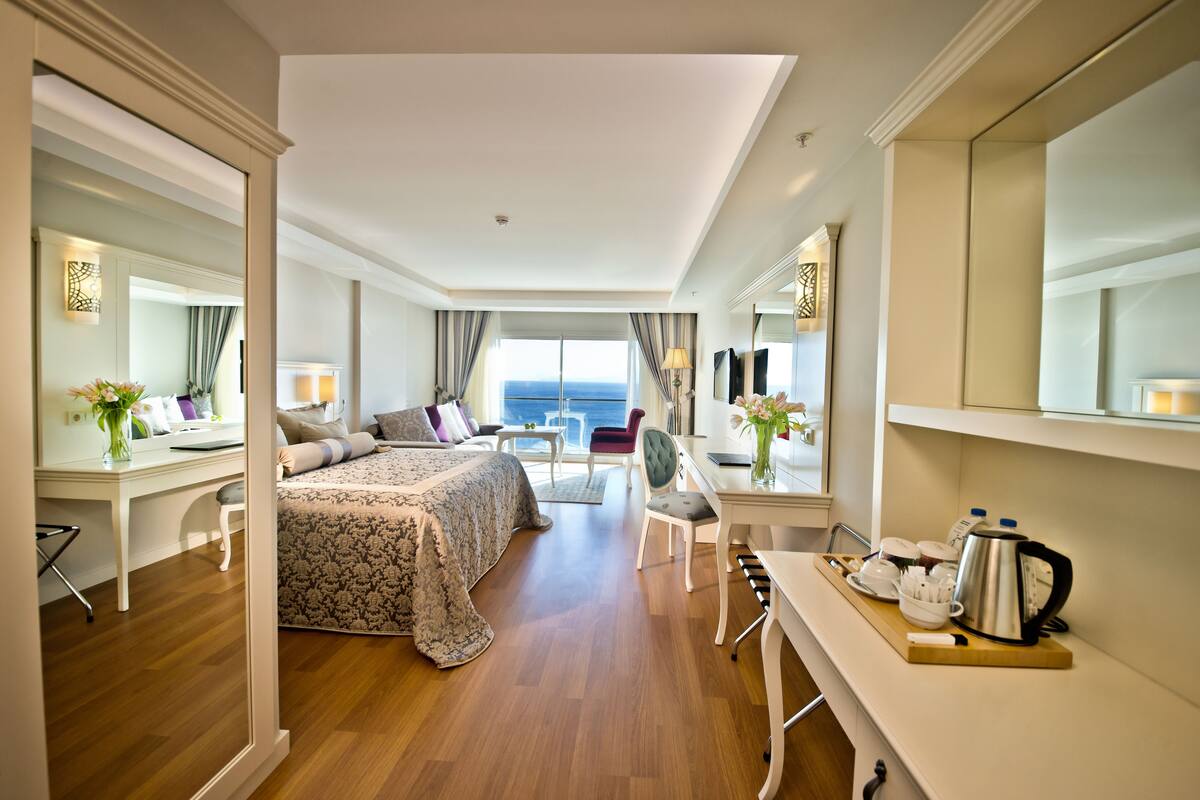 A modern hotel room with a large bed, a desk, a chair, and a view of the sea.