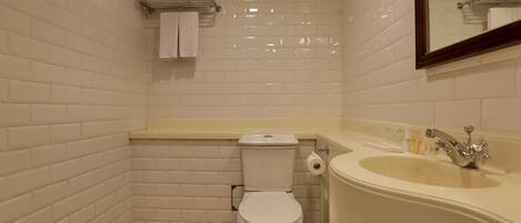 A bathroom with white tiled walls, a white toilet, a beige sink with a chrome faucet, and a mirror above the sink.