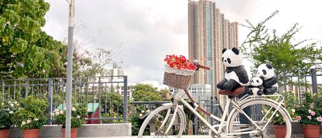 A bicycle with a basket of flowers and two panda plush toys, parked on a sidewalk with a street sign and buildings in the background.