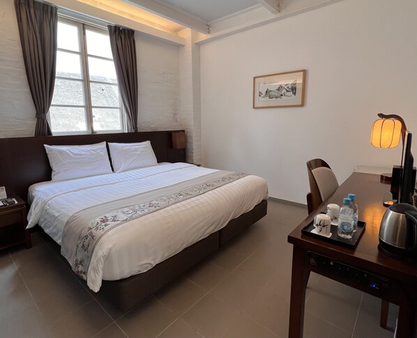 Une chambre d’hôtel avec un grand lit, une table de chevet avec une lampe, une chaise et une petite table sur laquelle se trouvent une bouilloire et des bouteilles.