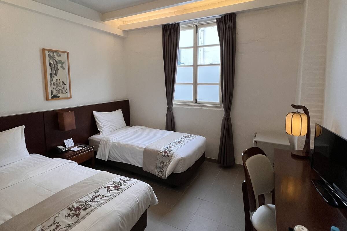 Une chambre d’hôtel avec deux lits, un bureau, une chaise, une télévision et une fenêtre avec des rideaux.