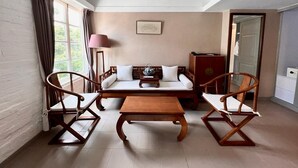 Une pièce confortable avec un canapé, deux chaises en bois, une petite table et une lampe.