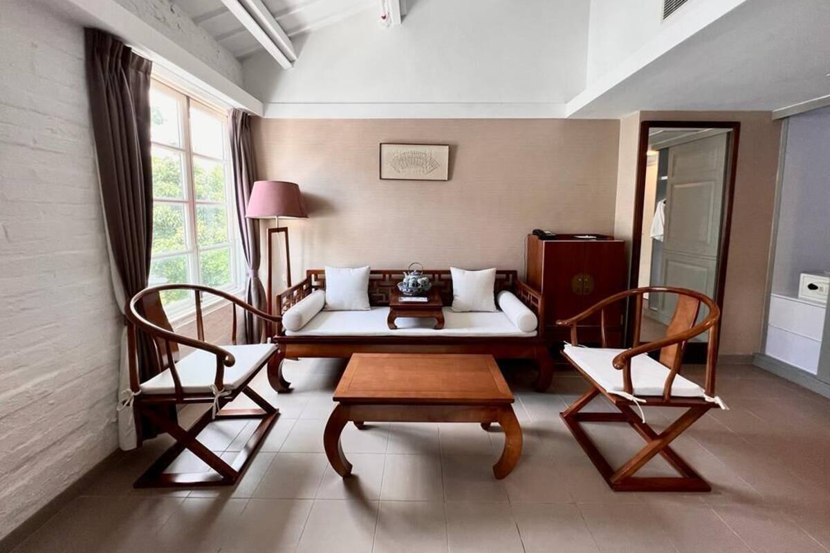 Une pièce confortable avec un canapé, deux chaises en bois, une petite table et une lampe.
