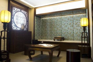 A traditional room with a wooden table, two floor lamps, a window with a decorative screen, and a small bench.