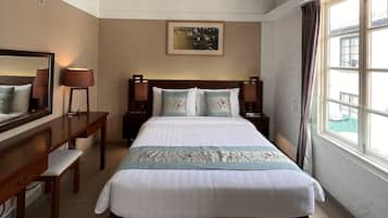 Une chambre d’hôtel avec un grand lit, un bureau et une chaise. Il y a une fenêtre avec des rideaux et un tableau au mur.