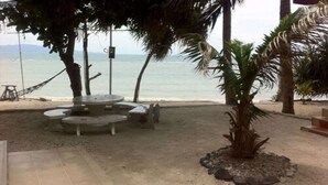 Une terrasse au bord de la plage, avec un espace salon circulaire, des palmiers et une vue sur la mer.