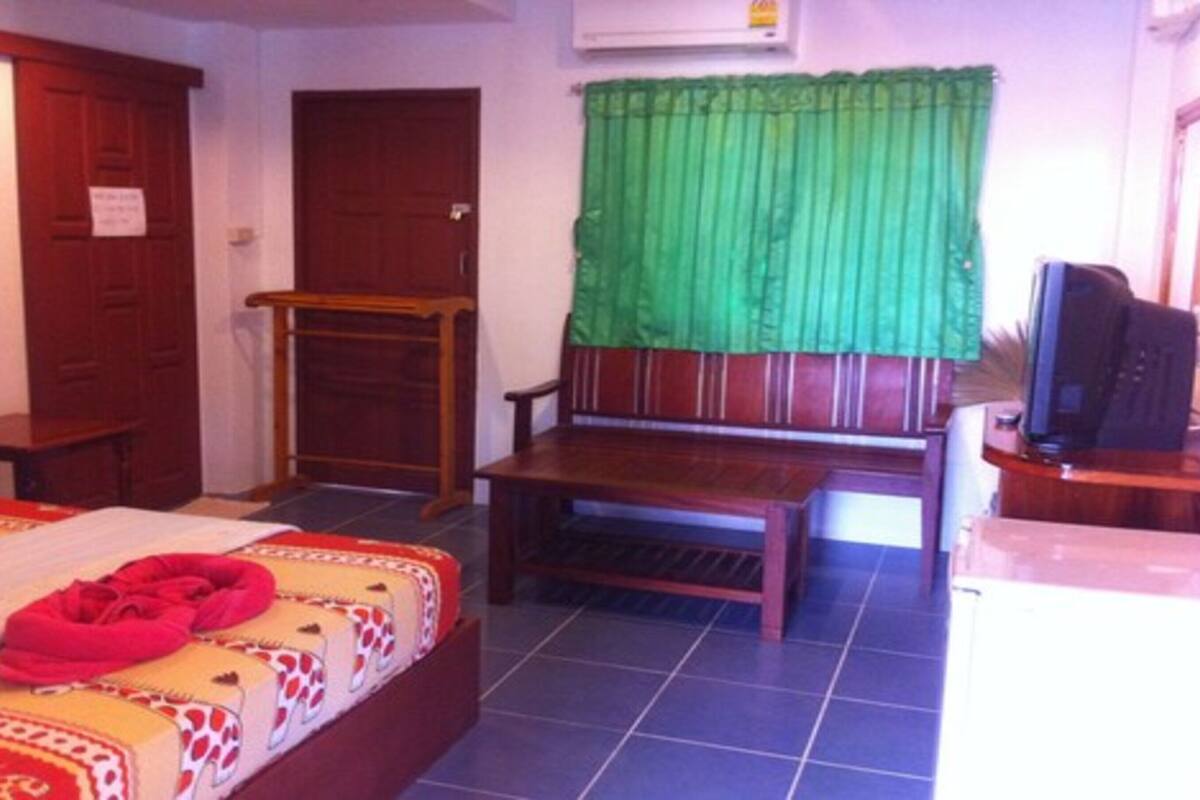 A room with a bed, a wooden bench, a television, and a green curtain.