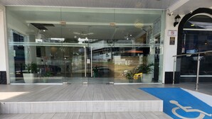 Moderne entree van een gebouw met glazen deuren, een blauwe hellingbaan voor mindervaliden en potplanten.