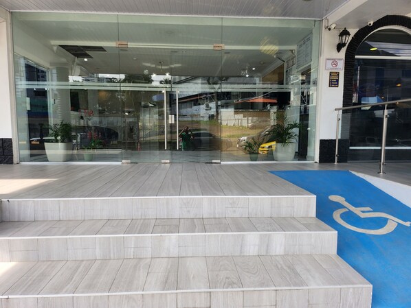 A modern building entrance with glass doors, a blue handicap-accessible ramp, and potted plants.