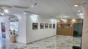 Een ruime lobby met marmeren vloer, ingelijste foto’s aan de muur en een receptiebalie met potplanten.