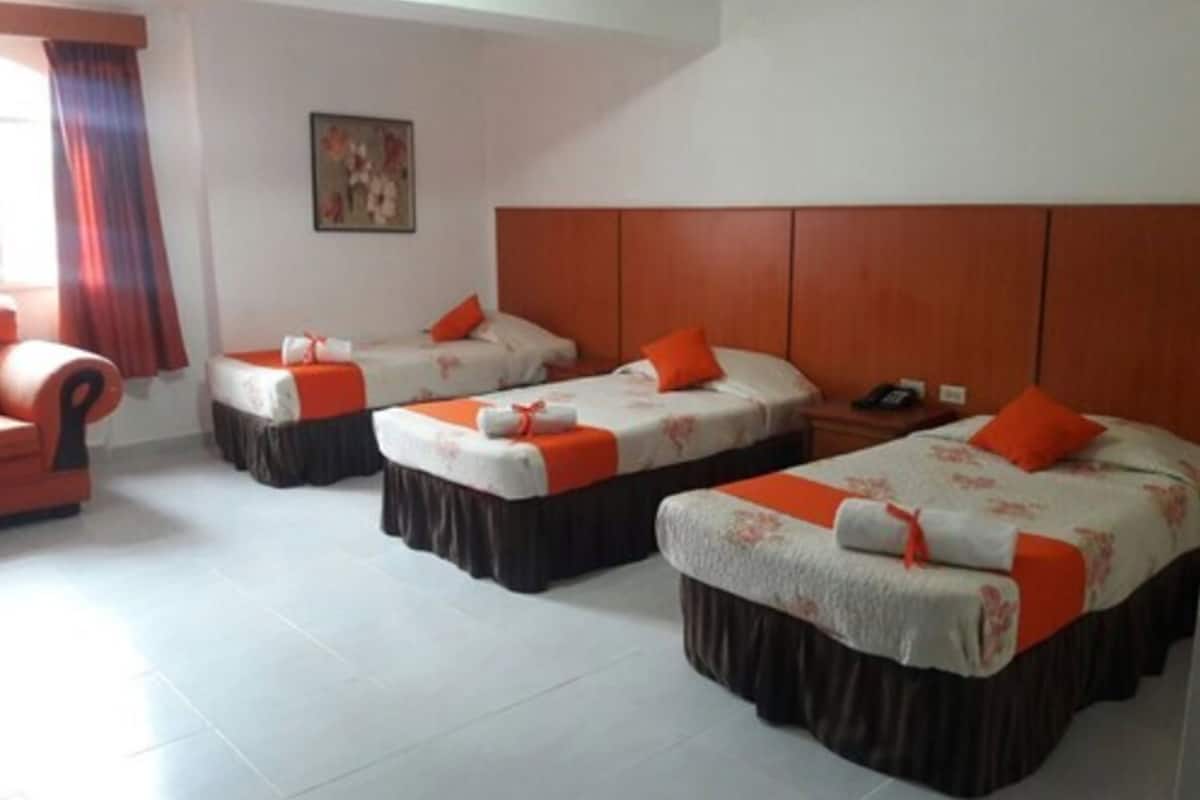Une chambre d’hôtel avec trois lits, chacun doté d’une tête de lit marron et d’oreillers orange. On y trouve également une tête de lit en bois, un tableau au mur et une chaise.