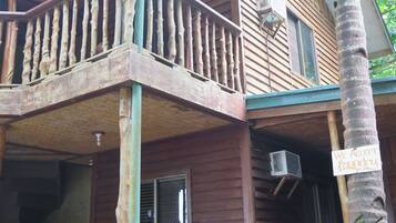 A wooden house with a balcony, a sign indicating laundry acceptance, and an air conditioning unit.