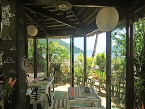 A room with a thatched roof, wooden furniture, and a view of a tropical landscape.
