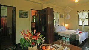 Hotelkamer met een bed, nachtkastje, een tafel met fruit en glazen, en een decoratieve plant.