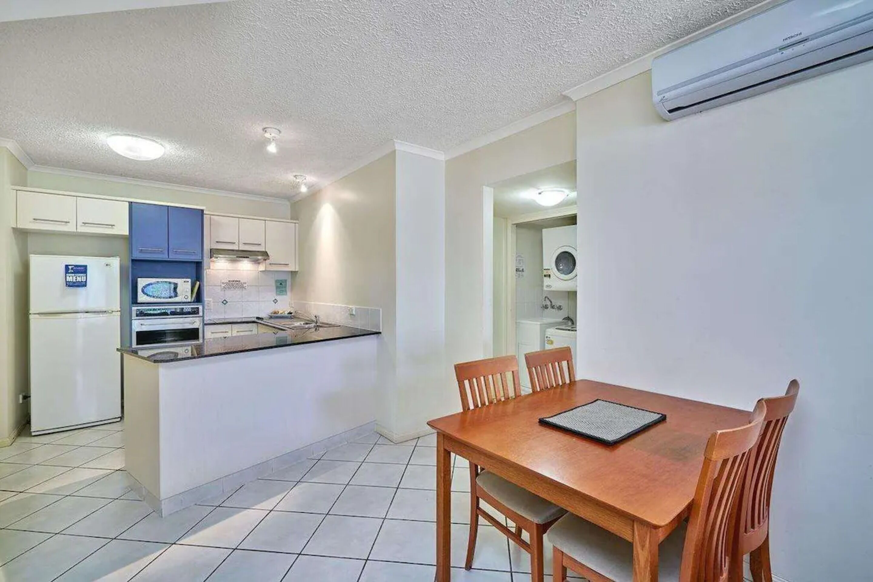 A compact kitchen with a dining area, white cabinets, a microwave, and an air conditioning unit.