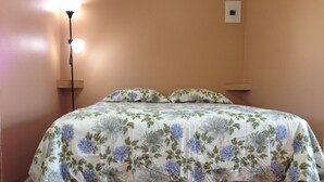 A bed with floral bedding, a bedside lamp, and a wall-mounted light switch. - Relax Inn (Streator)