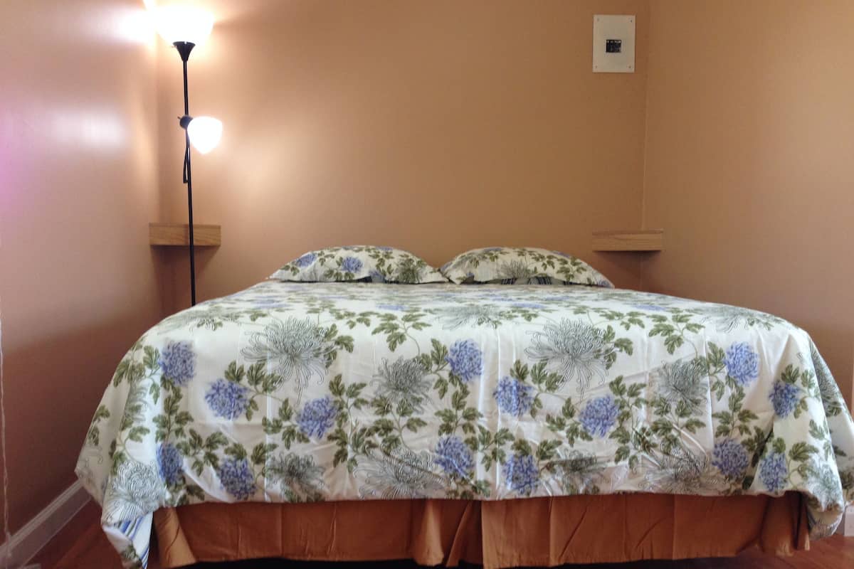 A bed with floral bedding, a bedside lamp, and a wall-mounted light switch.