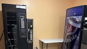 A room with a vending machine, a small table, and a wall-mounted refrigerator. - Relax Inn (Streator)