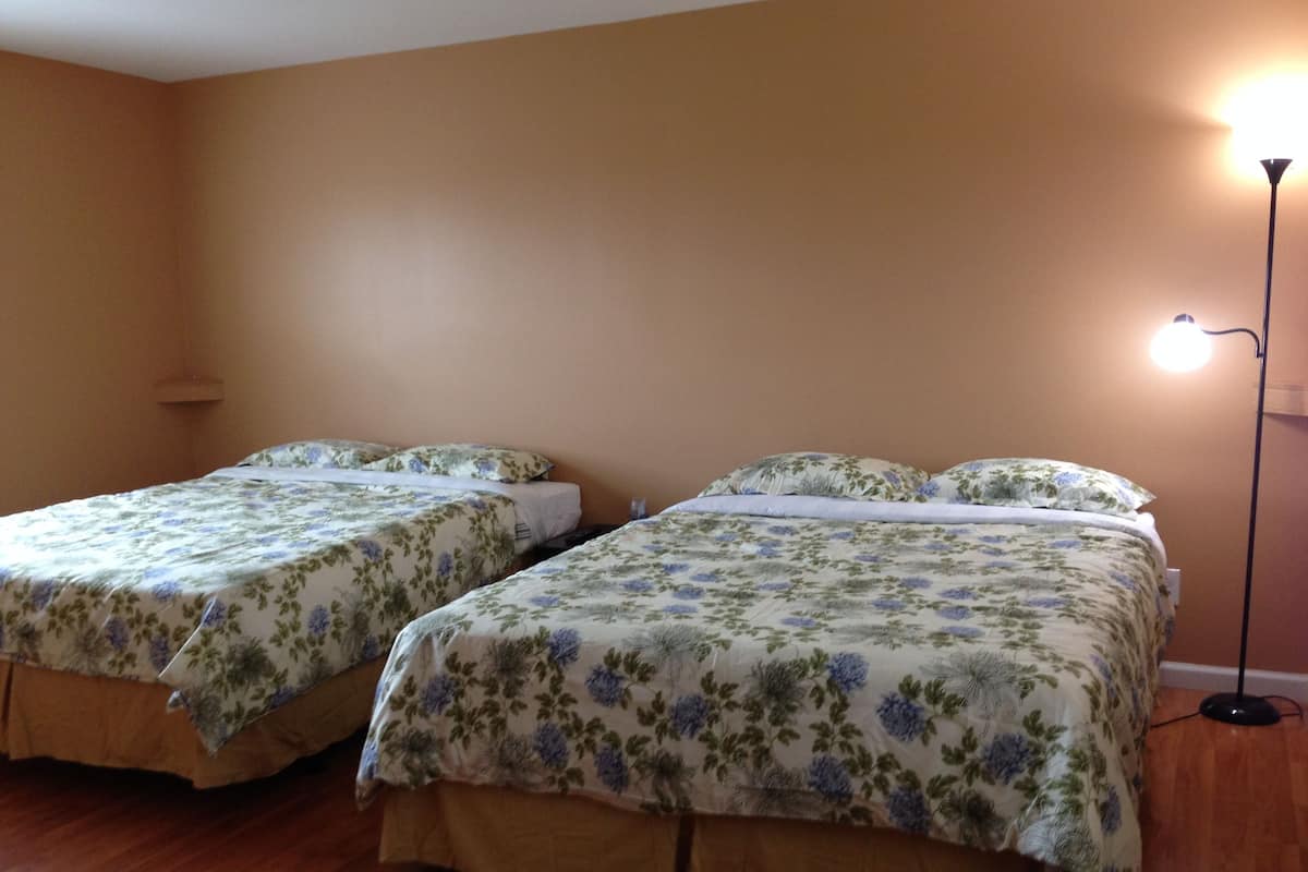 A room with two beds, each with floral bedding, a floor lamp, and a wooden floor.