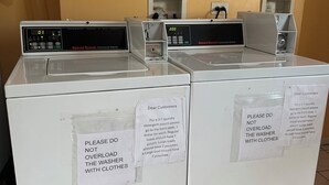 A row of white commercial washers with instructions taped to them. - Relax Inn (Streator)