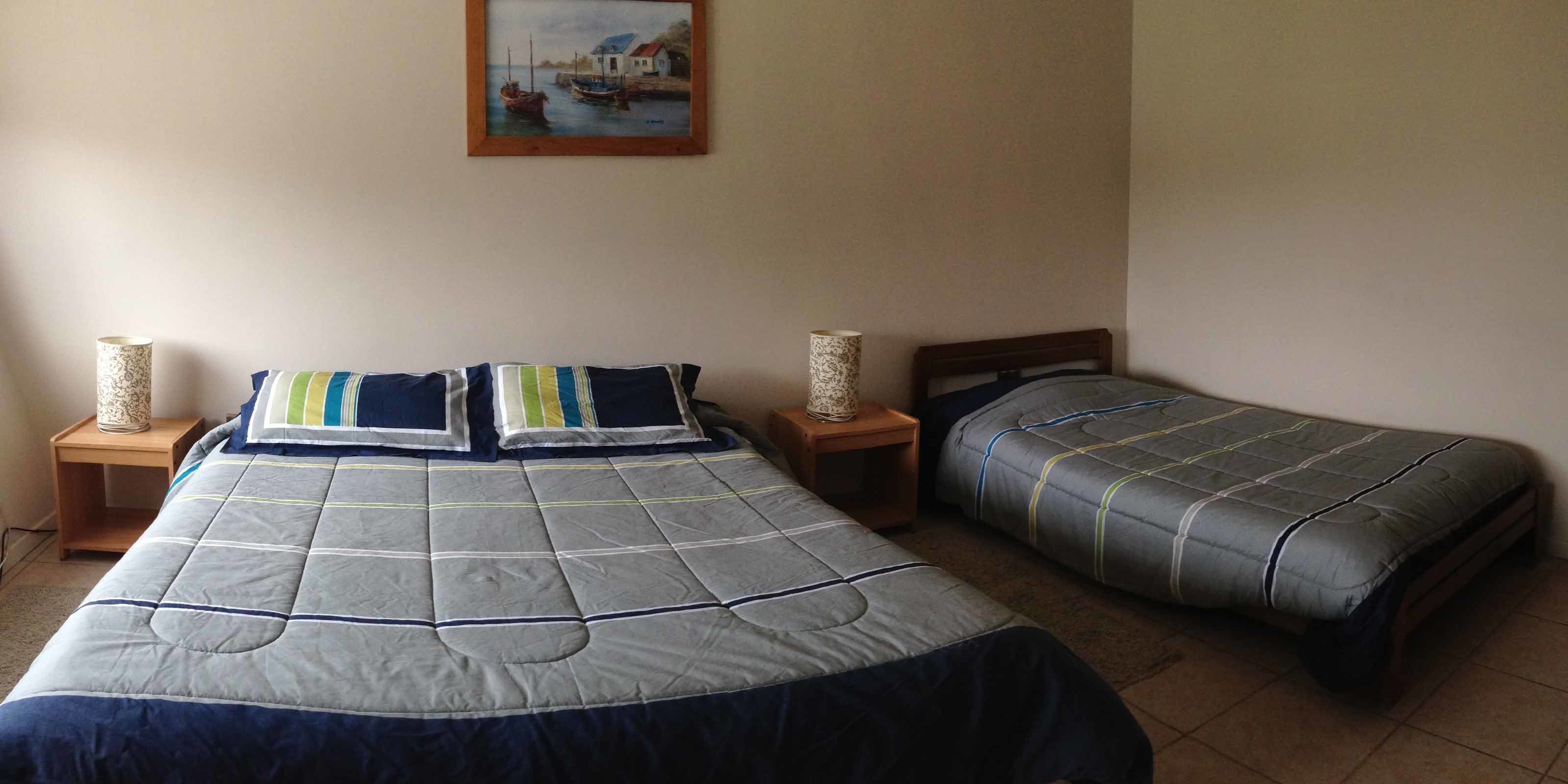 A bedroom with two single beds, a painting on the wall, and two bedside tables with lamps.
