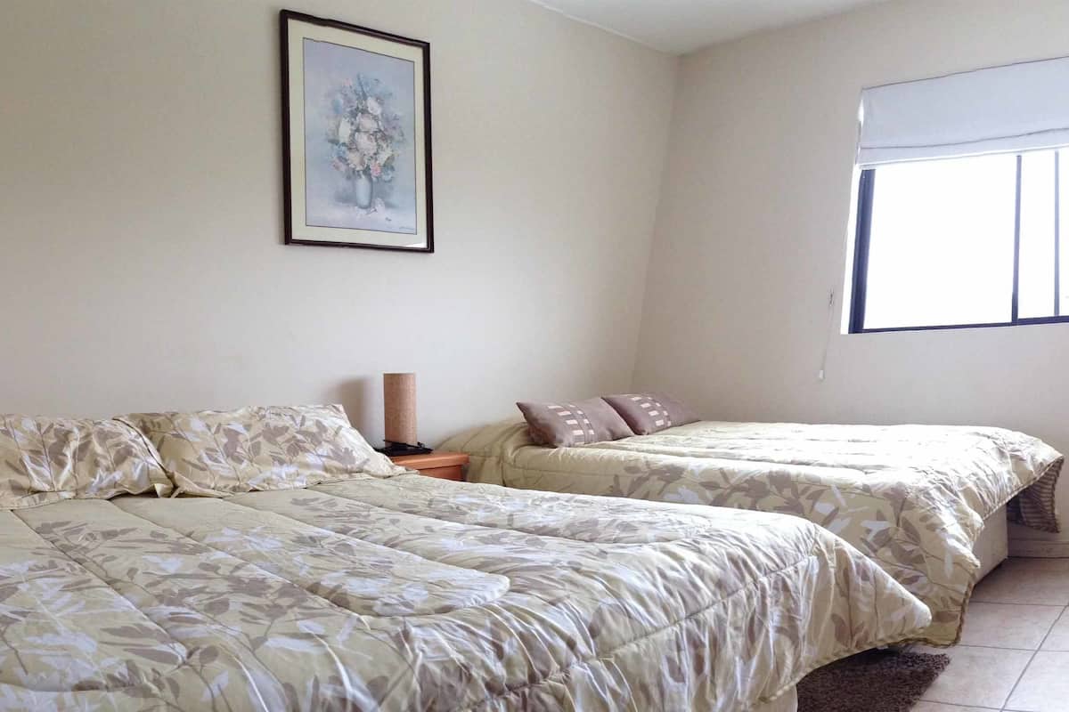 A bedroom with two beds, a framed picture on the wall, and a window with a blind.