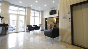 Un vestíbulo moderno con entrada por puerta de vidrio, un televisor de pantalla plana en la pared y un mostrador de recepción.