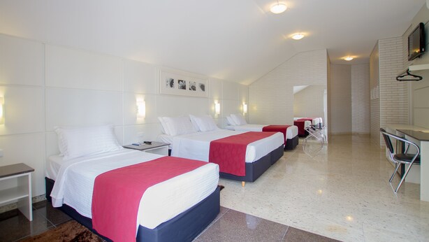 Habitación de hotel con tres camas, una mesita pequeña, una silla y un televisor montado en la pared.