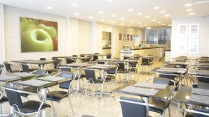 Un aula con escritorios y sillas dispuestas en filas, un gran trabajo artístico con forma de manzana en la pared y una zona de cocina al fondo.