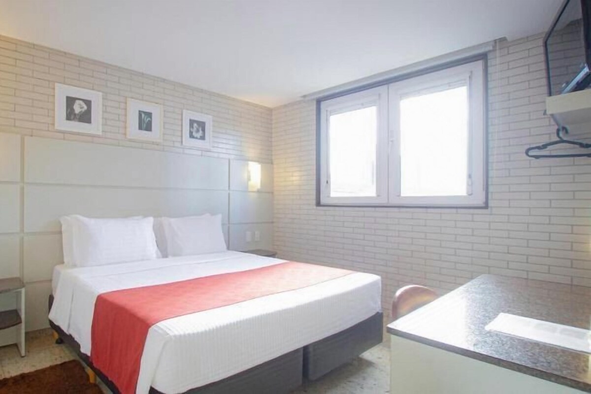 A hotel room with a bed, bedside table, and a desk with a chair.