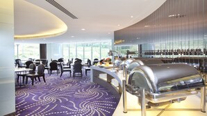 Un moderno vestíbulo de hotel con zona de comedor, ventanas amplias y presentación tipo bufé.