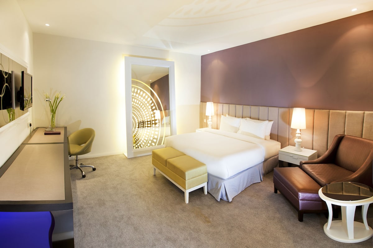 A modern hotel room with a large bed, a desk, a chair, and a small table.