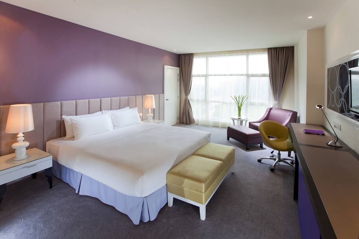 A hotel room with a large bed, a desk with a chair, a television, and a window with curtains.